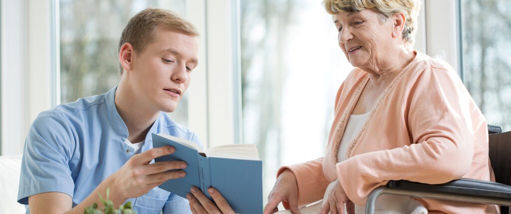 Ein Pfleger liest einer älteren Frau aus einem Buch vor
