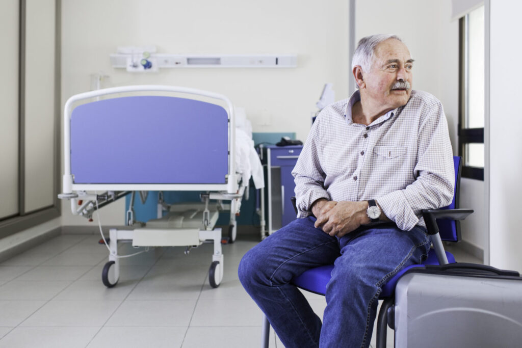 Ein älterer Mann sitzt in seinem Krankenzimmer und wartet auf seine Entlassung