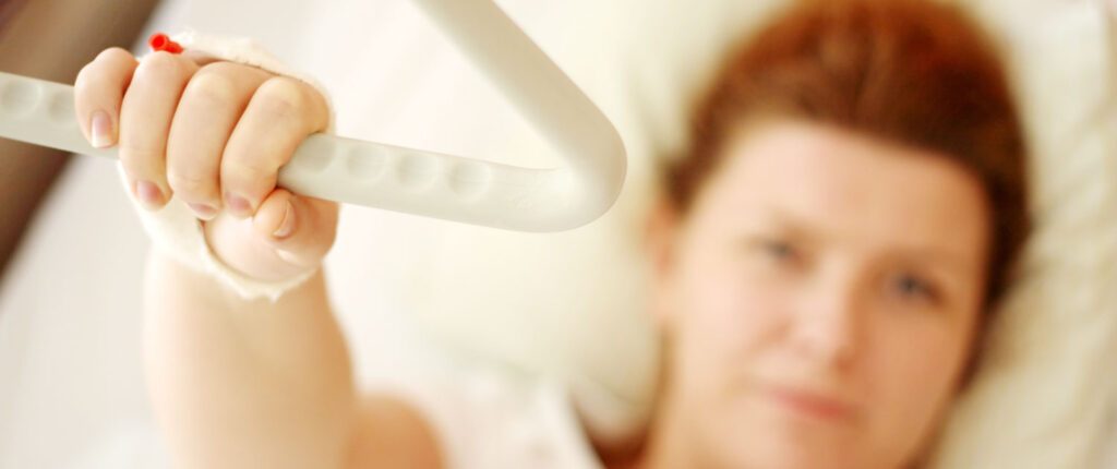 Frau in Krankenhausbett mit einer Hand an herabhängendem Handgriff