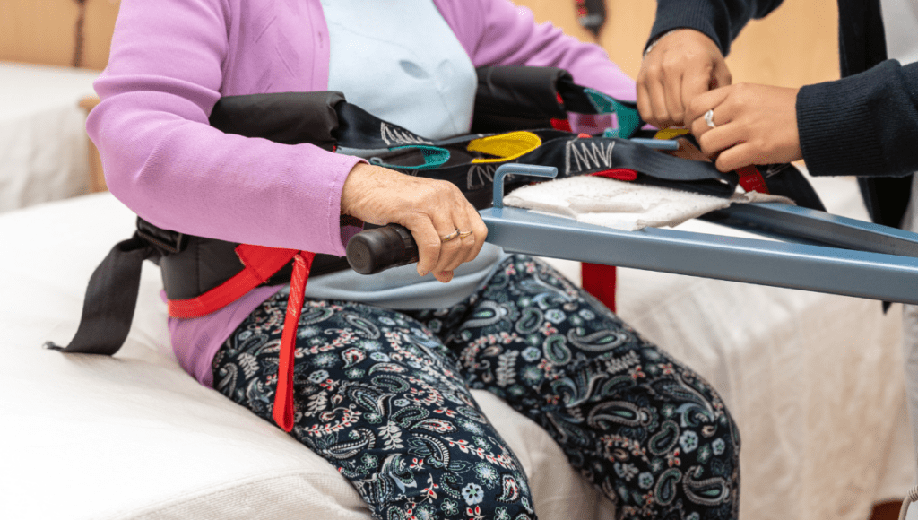 Eine pflegebedürftige Person wird mit einem Hilfsmittel aus dem Bett gehoben. Das erleichtert die Pflege.