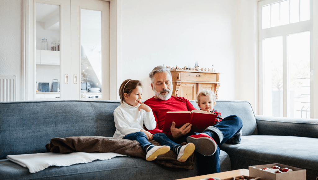 Ein normaler Alltag mit Stoma ist möglich, egal ob Ernährung, Sport oder Reisen: Hier sitzt ein Opa mit seinen Enkeln auf dem Sofa und liest ein Buch vor.