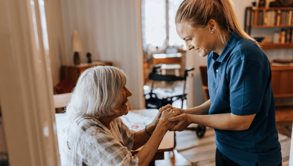 Eine ambulante Pflegeperson leistet eine bedürfnisorientierte Pflege bei einer alten Dame im Wohnzimmer.